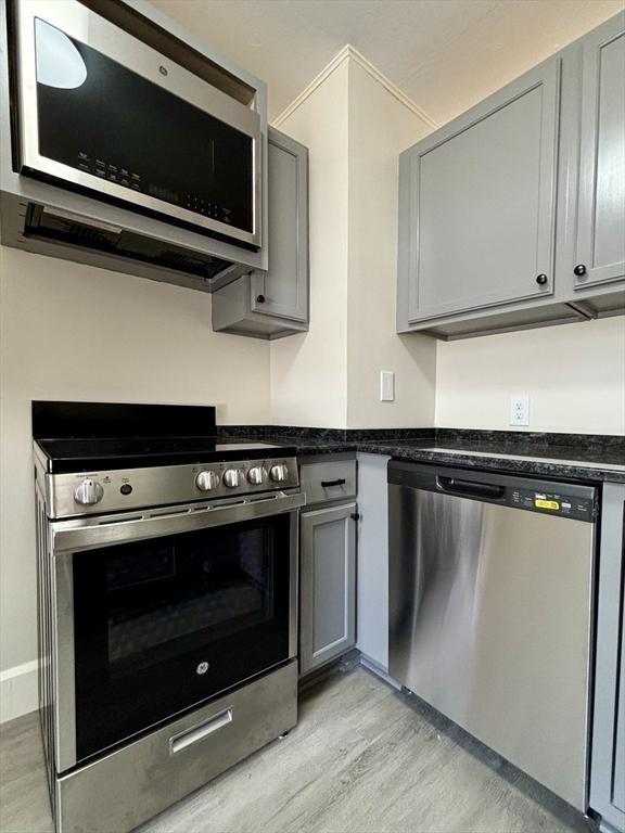 kitchen with stainless steel appliances, gray cabinetry, light wood-style flooring, and dark stone counters