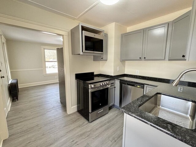 kitchen featuring dark stone countertops, light wood-style flooring, gray cabinets, a sink, and stainless steel appliances