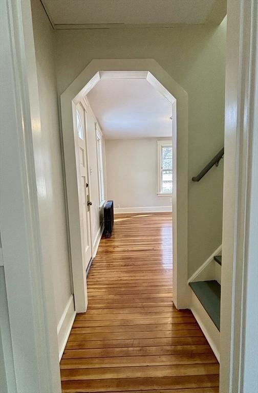 corridor with stairway, wood finished floors, arched walkways, and baseboards