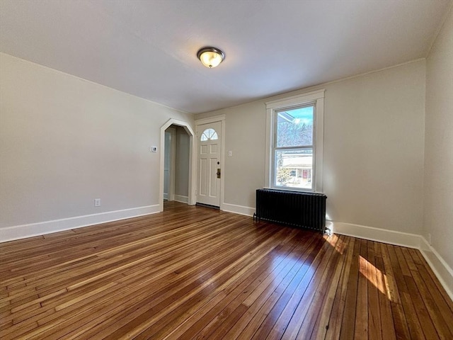 interior space featuring baseboards, arched walkways, dark wood-style floors, and radiator heating unit