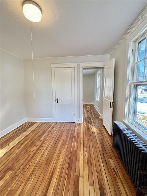 unfurnished bedroom with light wood-style flooring, radiator, ornamental molding, and multiple windows