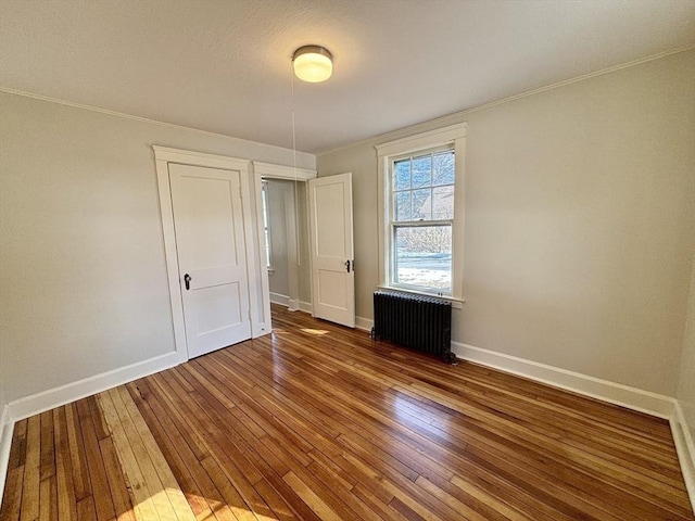 unfurnished bedroom featuring ornamental molding, radiator heating unit, baseboards, and wood-type flooring