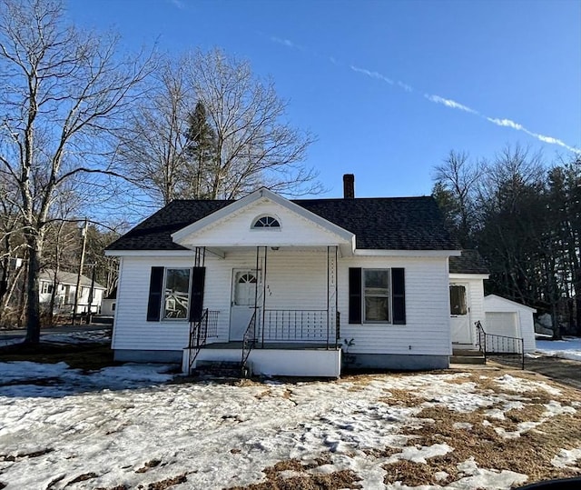 view of front facade featuring an outbuilding, covered porch, roof with shingles, and a chimney