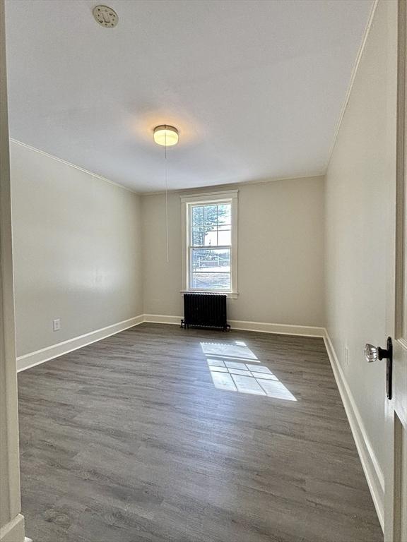 unfurnished room featuring crown molding, radiator heating unit, baseboards, and dark wood-style flooring