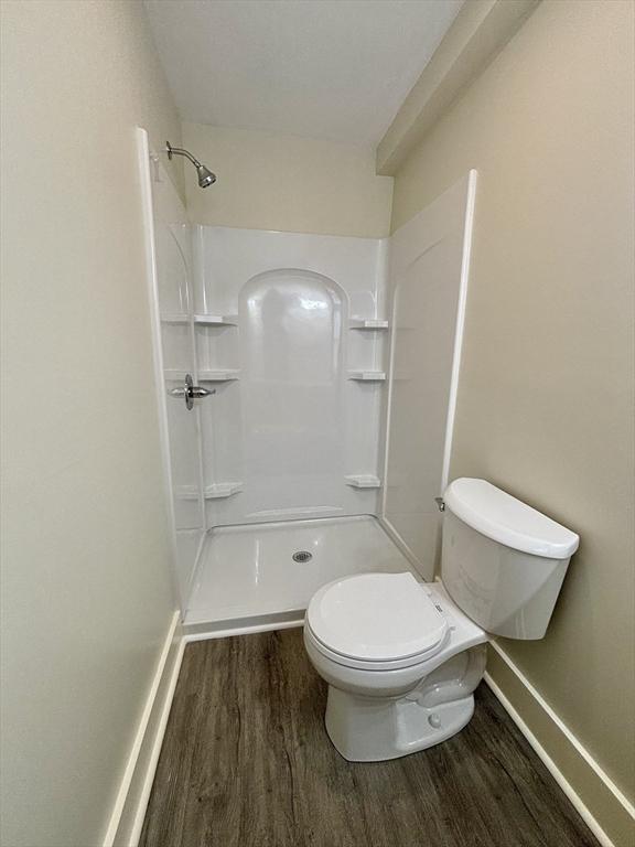 bathroom with toilet, a shower, baseboards, and wood finished floors