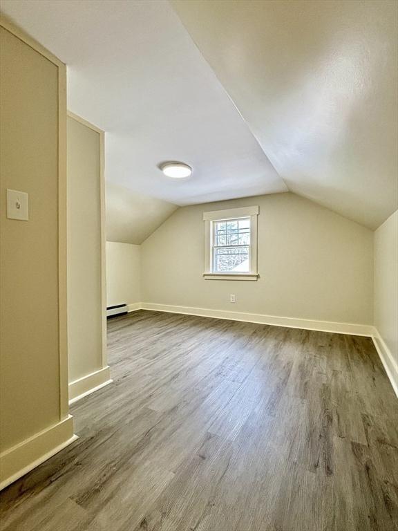 additional living space featuring dark wood finished floors, lofted ceiling, baseboards, and a baseboard radiator