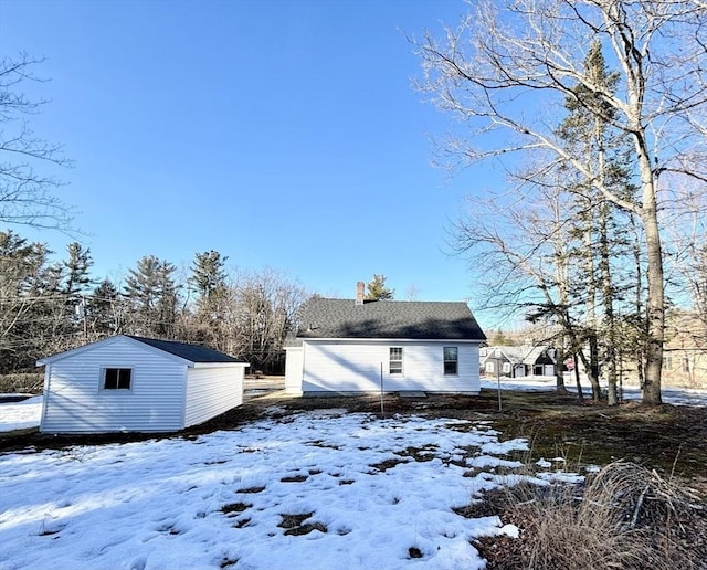 snow covered back of property with an outbuilding and a chimney