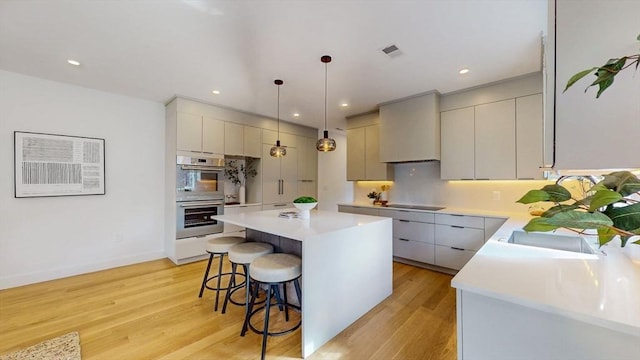 140 Columbia St Unit 2, Brookline, MA 02446 - kitchen featuring stainless steel double oven, black electric cooktop, a kitchen bar, light countertops, and recessed lighting