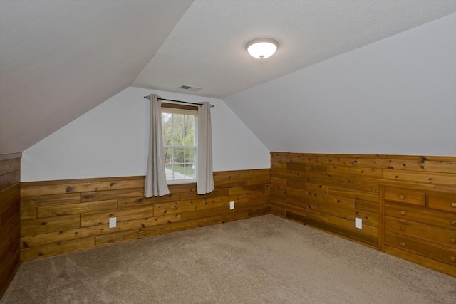 additional living space with visible vents, wood walls, wainscoting, carpet flooring, and vaulted ceiling