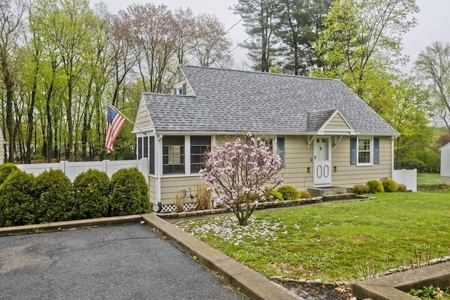 view of front facade featuring a sunroom, a shingled roof, a front lawn, and fence
