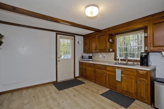 kitchen featuring brown cabinets, a sink, light wood finished floors, light countertops, and stainless steel microwave