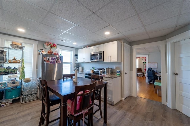 kitchen with white cabinets, appliances with stainless steel finishes, light hardwood / wood-style flooring, and a paneled ceiling