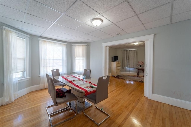 dining space featuring light wood-type flooring, a healthy amount of sunlight, and a drop ceiling