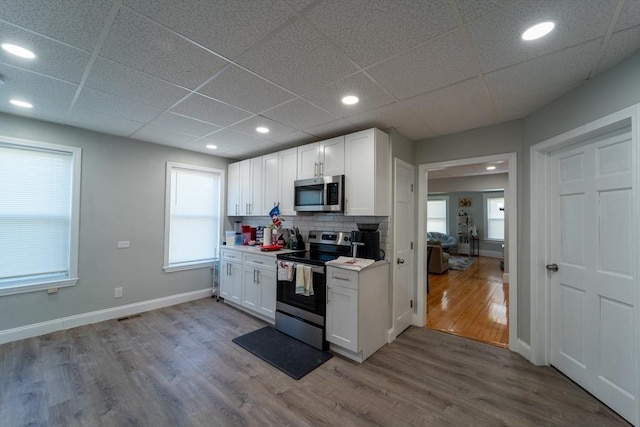 kitchen with white cabinets, appliances with stainless steel finishes, a paneled ceiling, decorative backsplash, and light wood-type flooring