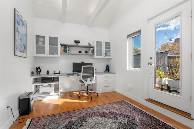 office area featuring light wood-type flooring, lofted ceiling with beams, and built in desk