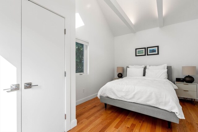 bedroom with lofted ceiling with beams and light hardwood / wood-style flooring