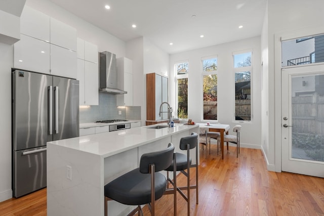 kitchen with stainless steel appliances, wall chimney range hood, sink, and an island with sink