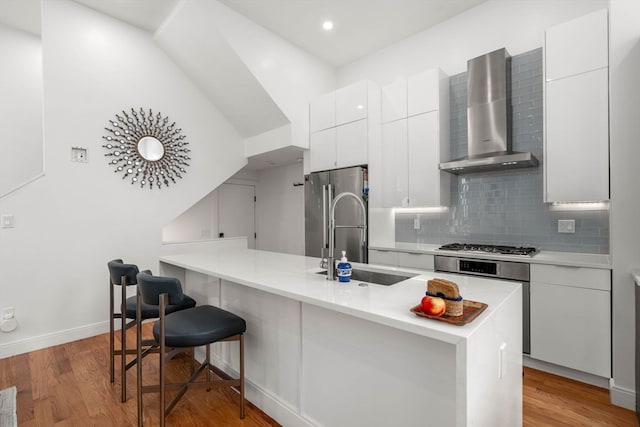 kitchen featuring white cabinets, a kitchen breakfast bar, wall chimney range hood, backsplash, and light wood-type flooring