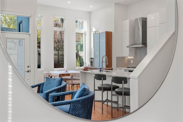 kitchen featuring hardwood / wood-style flooring, white cabinetry, sink, tasteful backsplash, and wall chimney range hood