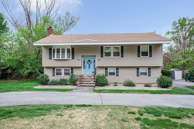 split foyer home featuring a chimney, a shed, a front yard, and an outdoor structure