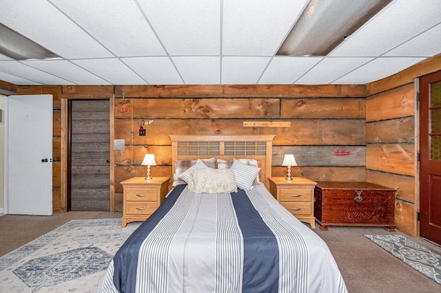 carpeted bedroom featuring a paneled ceiling and wooden walls