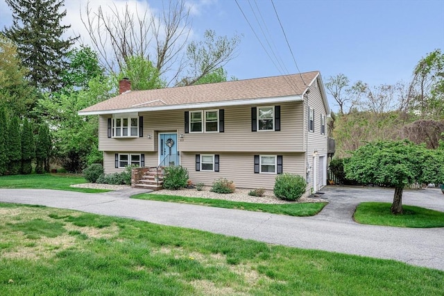 split foyer home featuring a chimney, driveway, a front yard, and an attached garage