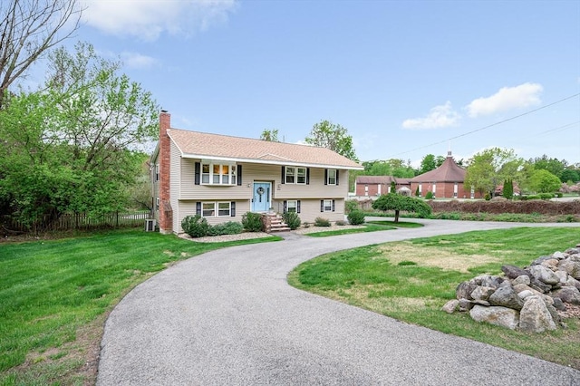raised ranch featuring a chimney, a front lawn, and asphalt driveway