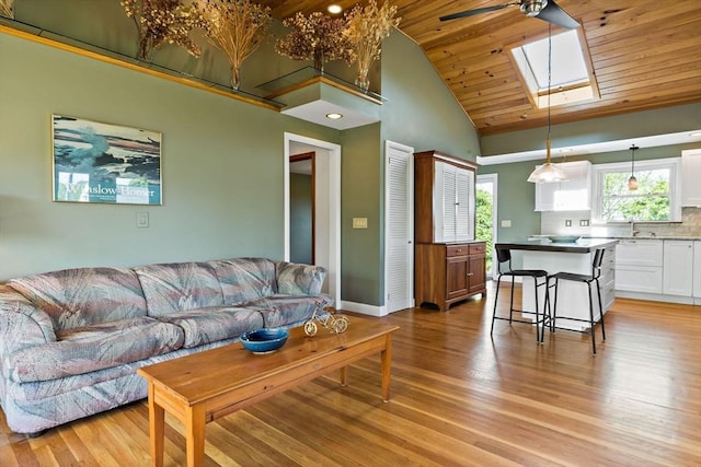 living area featuring a skylight, high vaulted ceiling, wooden ceiling, light wood-style flooring, and ceiling fan