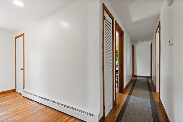 hallway featuring a baseboard radiator, wood finished floors, and baseboards
