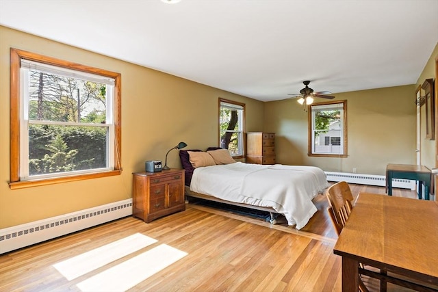 bedroom featuring a baseboard heating unit, light wood finished floors, and a ceiling fan