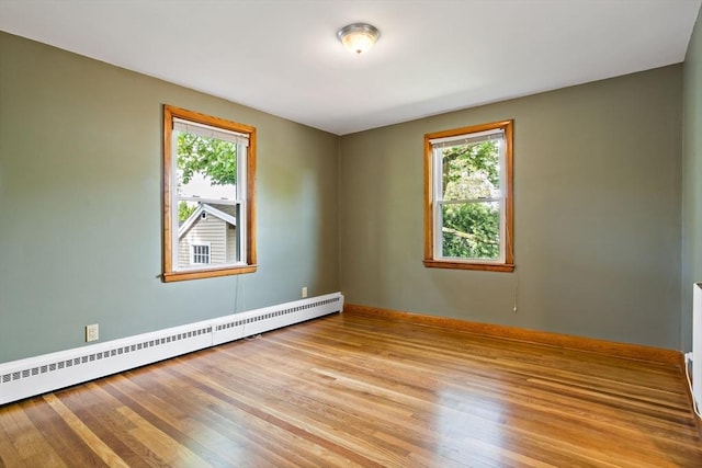 unfurnished room with a baseboard heating unit, healthy amount of natural light, and light wood-style flooring