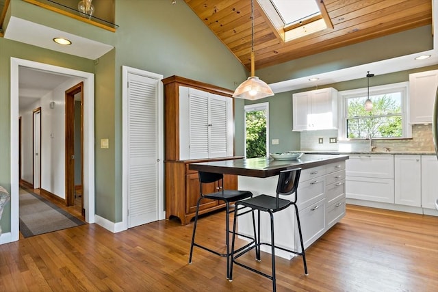 kitchen with a skylight, baseboards, white cabinets, light wood-style floors, and wood ceiling