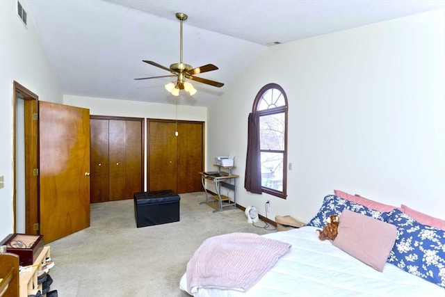 bedroom with visible vents, a ceiling fan, light colored carpet, vaulted ceiling, and multiple closets