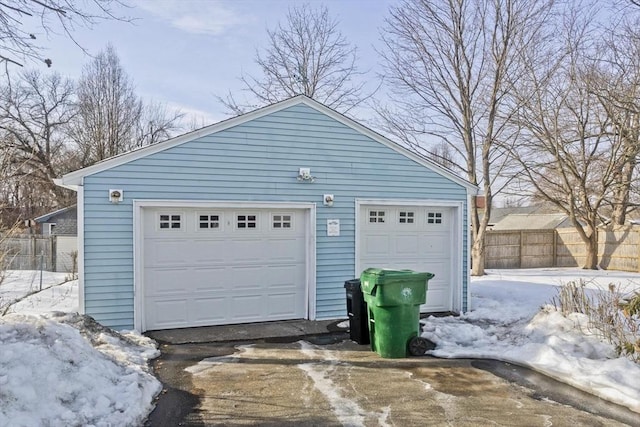 snow covered garage with a garage and fence