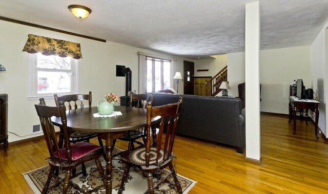 dining area featuring a wood stove, light wood finished floors, stairway, and a wealth of natural light