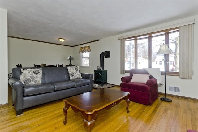 living room featuring crown molding, visible vents, a wood stove, light wood-type flooring, and baseboards