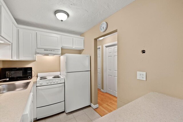 kitchen featuring under cabinet range hood, light countertops, white appliances, white cabinetry, and a sink