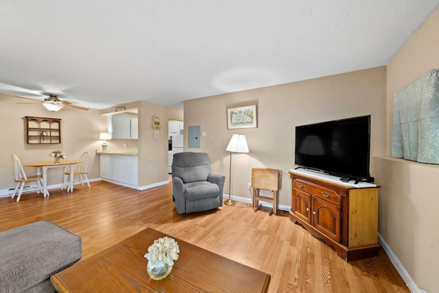 living area with electric panel, baseboards, and light wood-type flooring