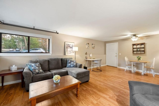 living area featuring baseboards, light wood-style flooring, and a ceiling fan