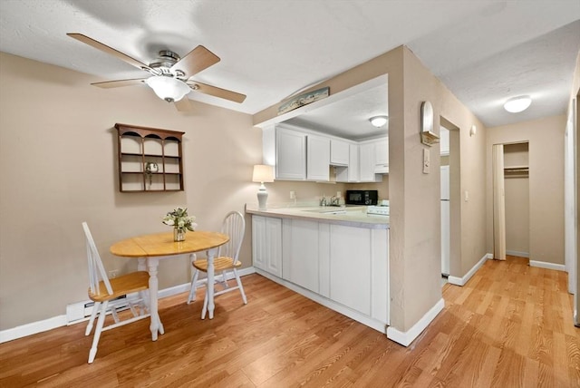 kitchen featuring light wood-style flooring, white cabinets, black microwave, light countertops, and baseboards