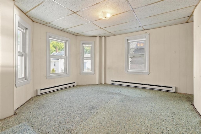 empty room with baseboard heating, a drop ceiling, and carpet