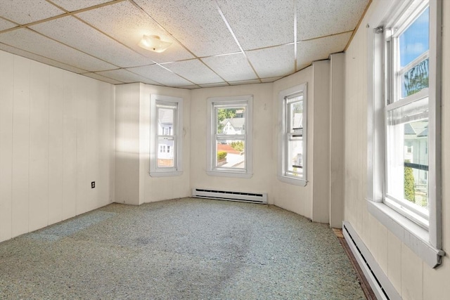carpeted empty room featuring a baseboard heating unit and a drop ceiling