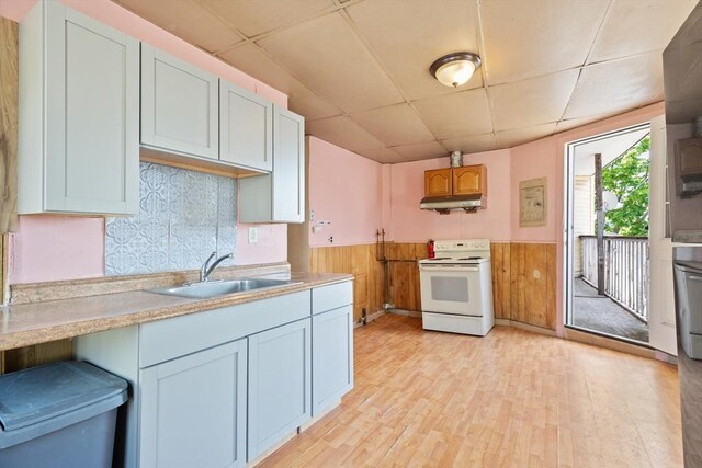 kitchen featuring electric range, a paneled ceiling, under cabinet range hood, a sink, and wainscoting