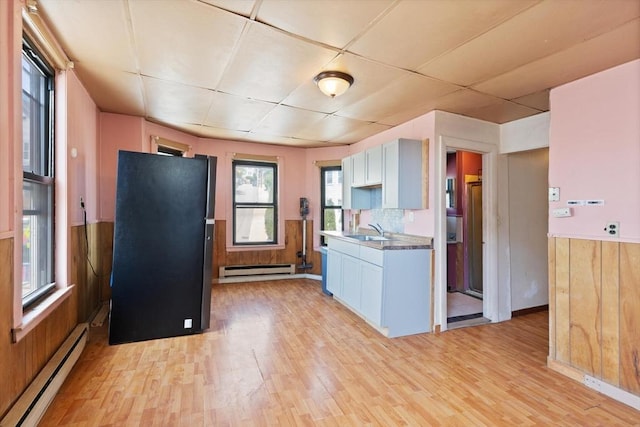 kitchen with a baseboard heating unit, light wood-style floors, a baseboard radiator, a sink, and wainscoting