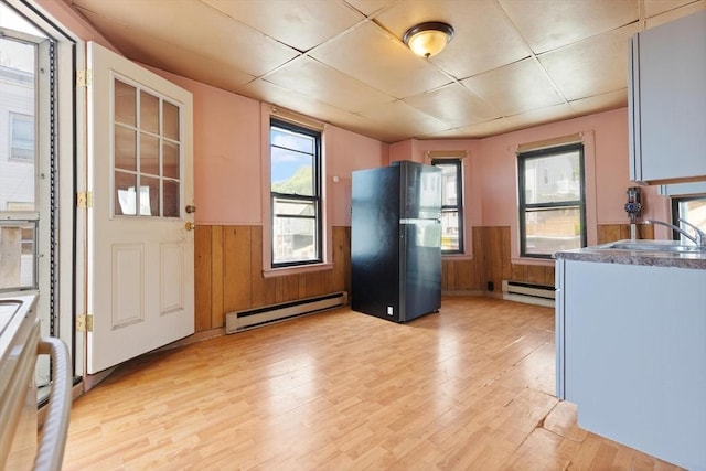 kitchen featuring a baseboard radiator, freestanding refrigerator, a sink, a wainscoted wall, and a paneled ceiling