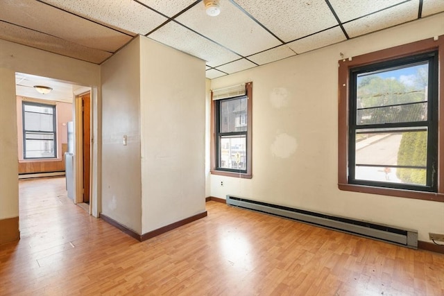 unfurnished room with a baseboard radiator, a drop ceiling, light wood-style floors, and a smoke detector