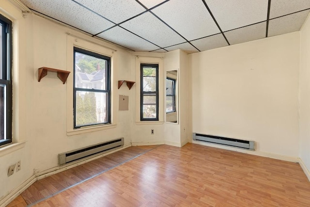 empty room with baseboard heating, a drop ceiling, wood finished floors, and baseboards