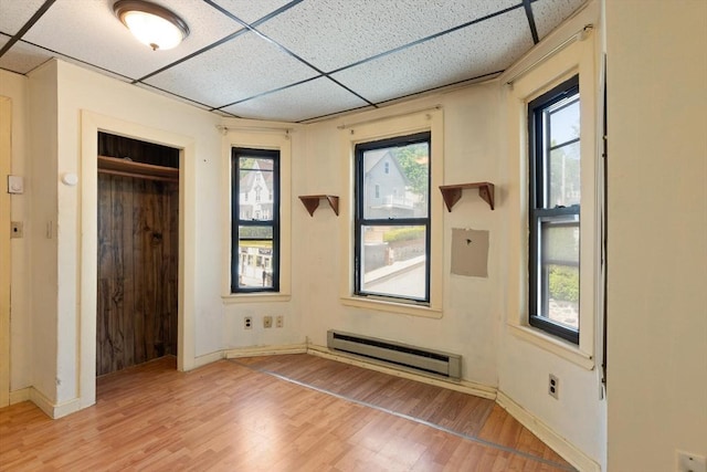 unfurnished bedroom with a baseboard radiator, a drop ceiling, light wood finished floors, baseboards, and a closet