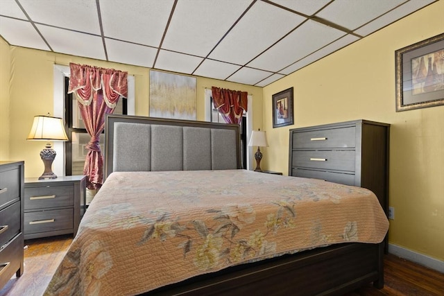 bedroom featuring wood finished floors, a drop ceiling, and baseboards
