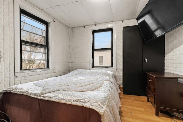 bedroom with light wood-style floors, multiple windows, and brick wall